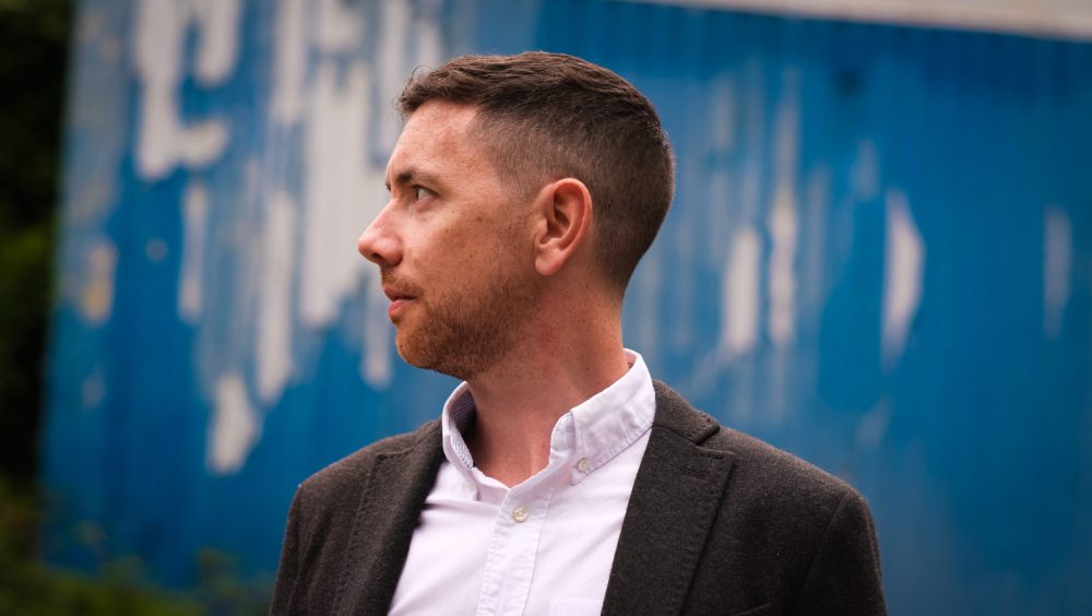 Man in profile facing left in front of a blue background