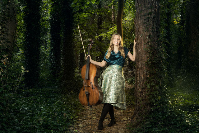 musician stands in a forest holding her cello