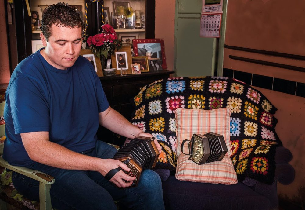 Man in a blue tshirt plays the concertina in a living room