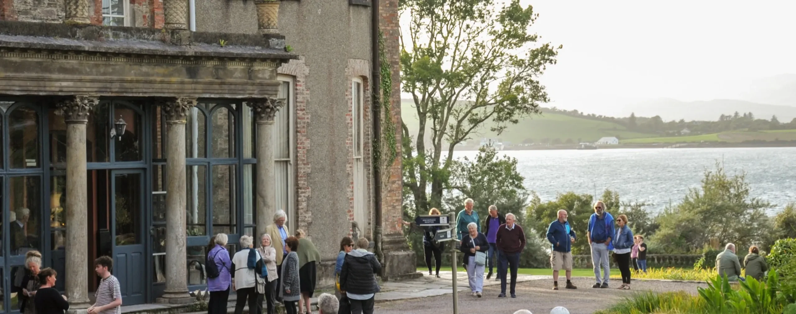 Visitors gathered outside Bantry House overlooking a lakeside landscape