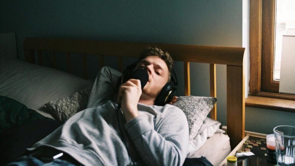 isaac jones lying in a bed holding a microphone wearing headphonew