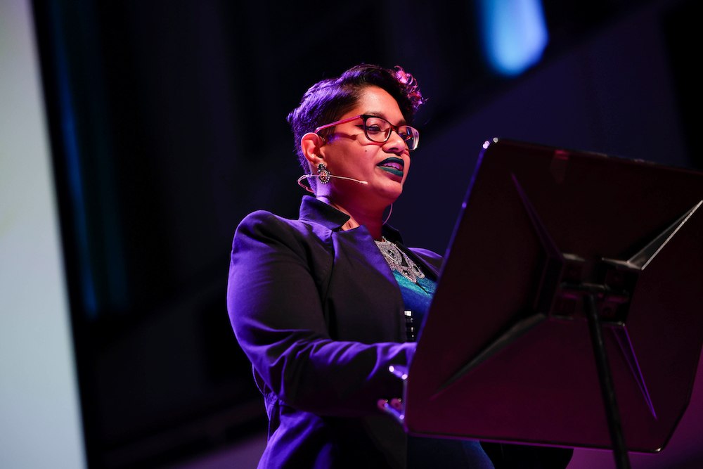 Photo of Chandrika Narayanan-Mohan on stage standing at a lectern